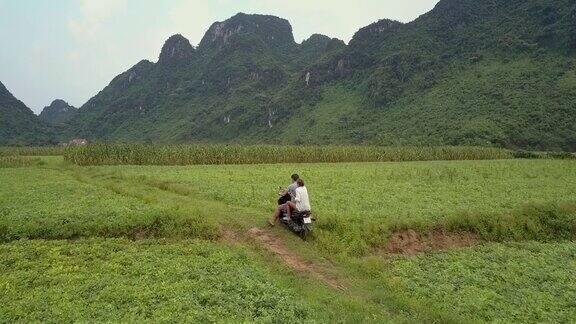 夫妇骑摩托车沿着崎岖的道路在田野鸟瞰