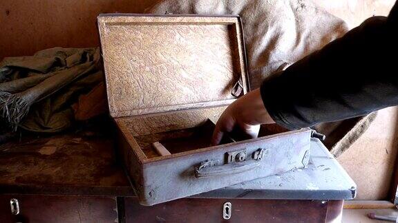 一个白人男子把一个满是灰尘的旧箱子放在木桌上打开它