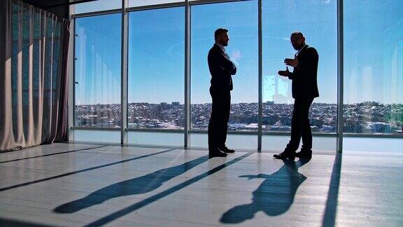 两个人的商务谈话穿着西装的企业家在宽敞的办公室里谈生意背景是窗户