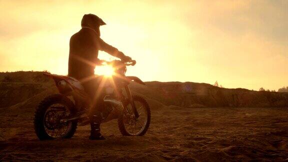 专业FMX摩托车骑手在他的摩托车上休息俯瞰坚硬的沙地越野地形太阳设置