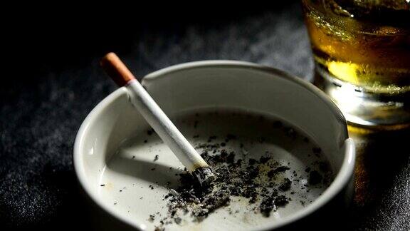 烟灰缸里点着的香烟和一杯威士忌的画面