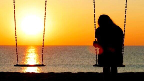 悲伤的女孩在海滩上荡秋千日落