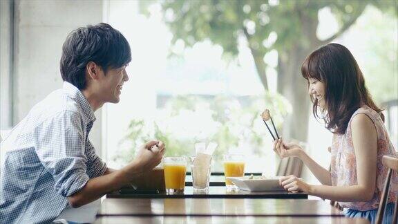 年轻的亚洲夫妇在餐厅用筷子品尝食物