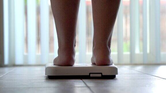 一个光着脚和腿的女人踩在浴室的秤上检查她的体重