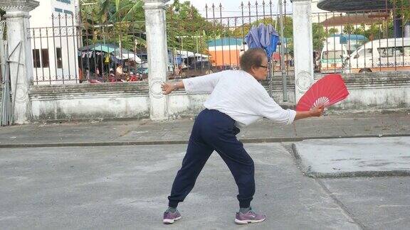 一位老妇人在停车场练习中国手扇子舞