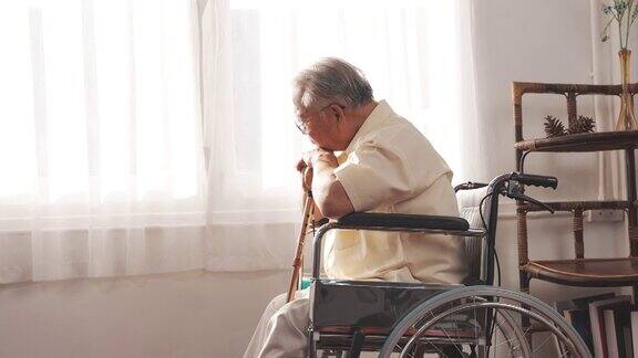 老年男性退休后独自呆在家里带着轮椅和拐杖看着窗外
