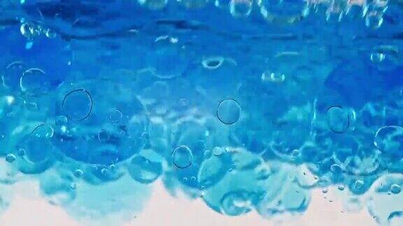 蓝色波浪水与泡沫在白色的背景清澈的蓝色水中的氧气泡泡矿泉水富含氧气的水缓慢的运动微距镜头