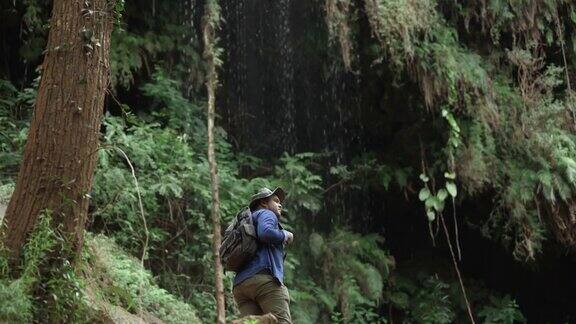 徒步旅行者正在热带雨林中旅行那里有美丽的瀑布年轻的亚洲人踏上了穿越森林的旅程双臂挺立欣赏大自然