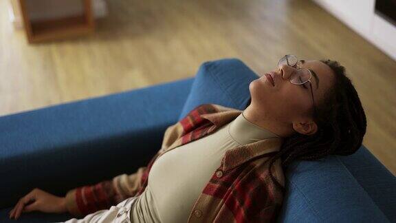 一位戴眼镜的非洲裔美国妇女筋疲力尽地躺在沙发上