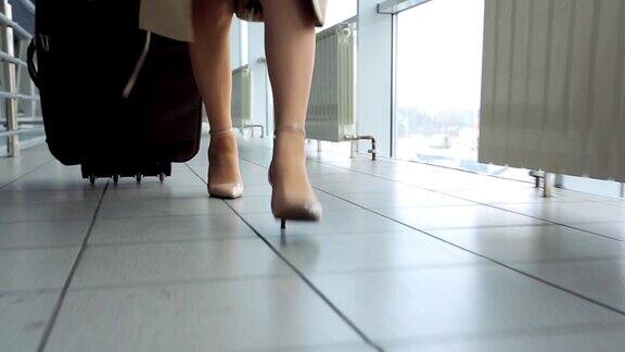 穿着高跟鞋的女人在机场用轮子推着行李箱