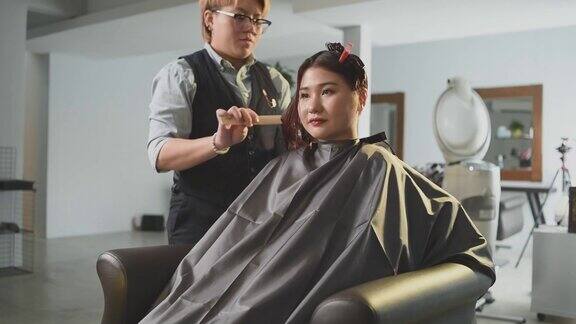慢动作美发沙龙亚洲华裔女性发型师在美发沙龙为她的顾客剪发梳理湿长发