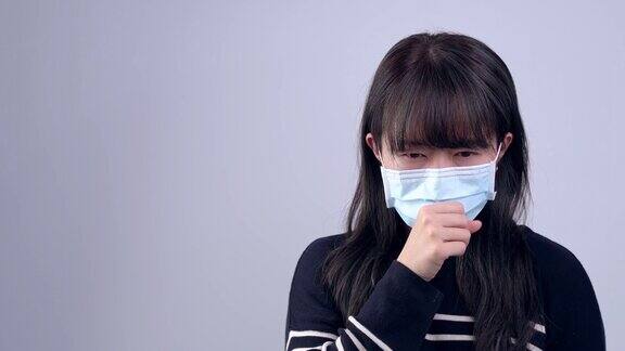 年轻女子咳嗽感觉不舒服戴着医用蓝色口罩灰色背景
