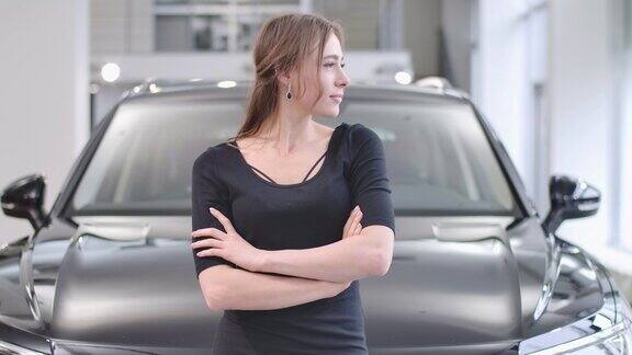 年轻的白人女孩的侧面肖像看着别处微笑着站在汽车经销商美丽的女人在新的黑色汽车前摆姿势汽车业务电影4k镜头ProRes总部