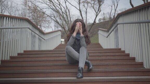 沮丧的白人女孩坐在城市公园的楼梯上哭泣美丽的黑发女人有问题悲伤沮丧悲伤压力
