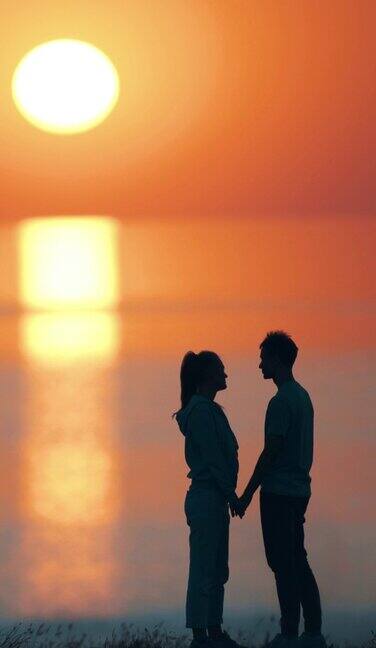 这对浪漫的情侣站在海边迎着美丽的夕阳