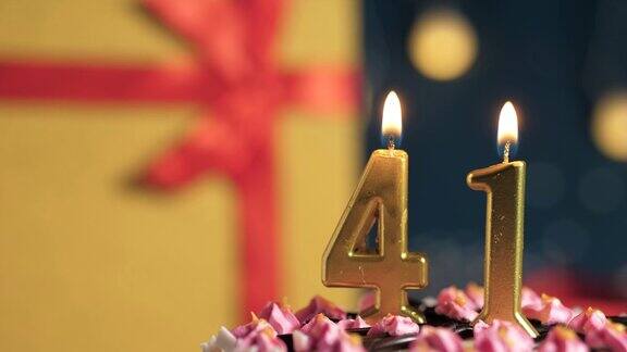 41号生日蛋糕用金色蜡烛点燃蓝色背景的礼物用黄色礼盒系上红丝带特写和慢动作