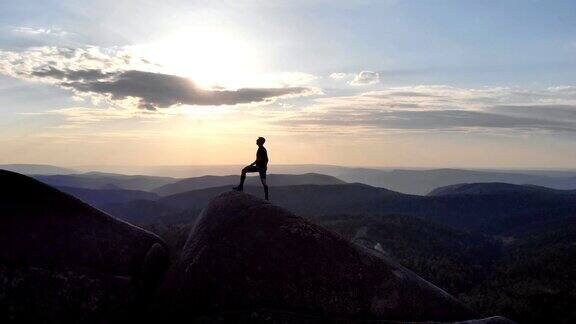 夕阳西下时一个人胜利地站在山顶上的剪影