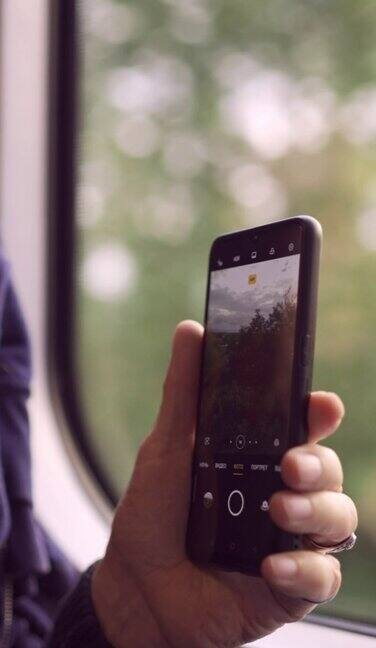 垂直视频-一个老人乘火车旅行的手特写用智能手机通过窗户拍摄风景