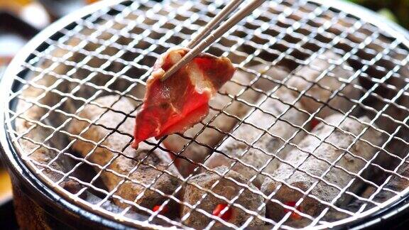 日本餐厅的炉子上放着用筷子夹着和牛烤肉的手