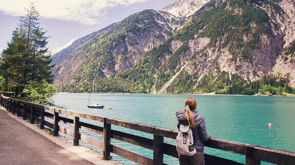女孩旅行者背着背包站在一个山的湖岸