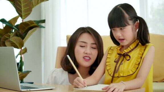 亚洲母亲帮助女儿在家里用笔记本电脑做作业