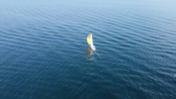 一艘挂着黄白帆的小帆船在蓝色的大海上航行海上旅游和暑假