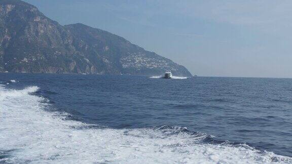 船尾有白色泡沫痕迹摩托艇漂浮在蓝色的海面上靠在丘陵的岸边意大利波西塔诺