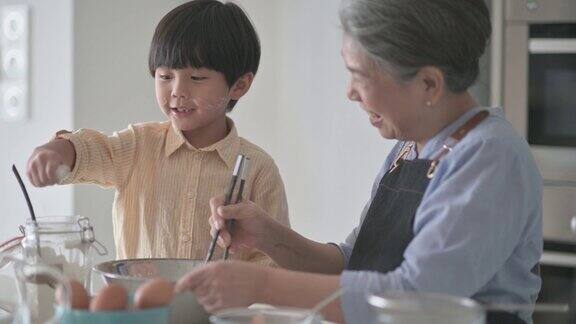 6岁的亚洲华人男孩在厨房柜台上用面粉烘焙帮助祖母准备食物