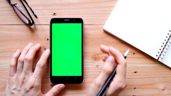 手用手机与绿色屏幕上的木制办公桌顶视图