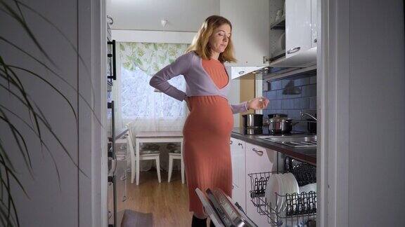 一个怀孕的女人在厨房里艰难地把洗好的盘子从洗碗机里拿出来
