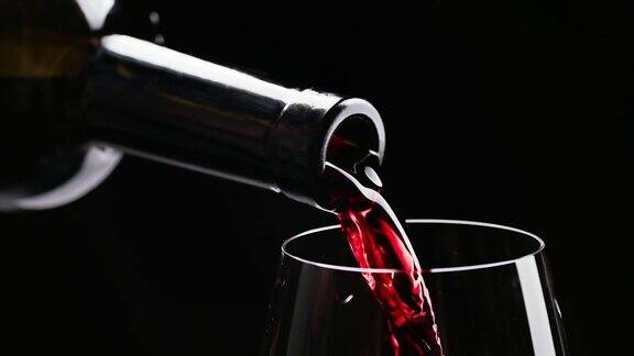 在黑色背景下红酒从酒瓶倒入高脚杯微距镜头