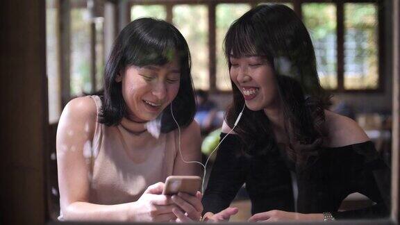 两个亚洲女性朋友使用智能手机分享在她的智能手机在咖啡馆