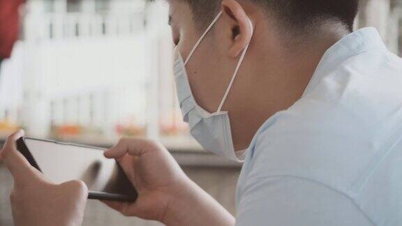 亚洲男孩戴着口罩坐在百货商店玩手机游戏新常态和社交距离的生活理念
