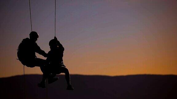 日落时分一对夫妇在山顶上的绳索攀爬队