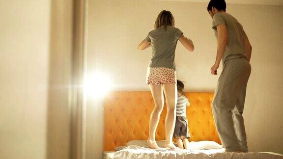 幸福的家庭和小儿子在晚上睡觉前在家里的床上跳舞