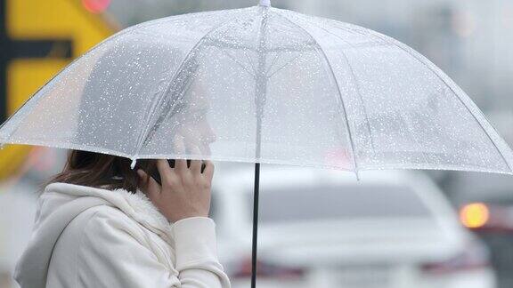 一名亚洲女子在雨天里站在城市街道上一边打手机一边撑着伞