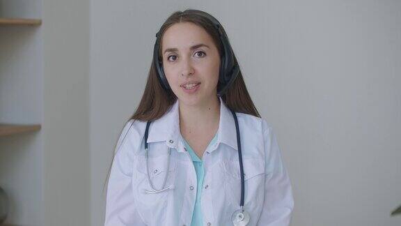 年轻的女医生面带微笑穿着白色制服听诊器通过视频电话在线咨询患者看着摄像头说话摄像头做远程视频聊天远程医疗和电子健康网络摄像头