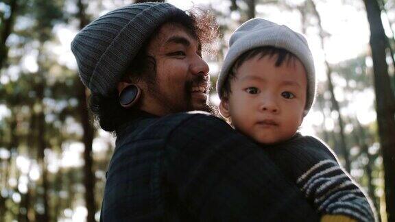 年轻的亚洲父亲在冬天抱着他的孩子在木头里