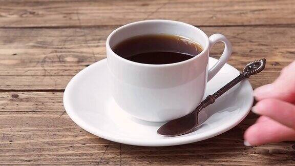 一个女人的手把一杯浓黑咖啡放在木桌上的茶托里近距离