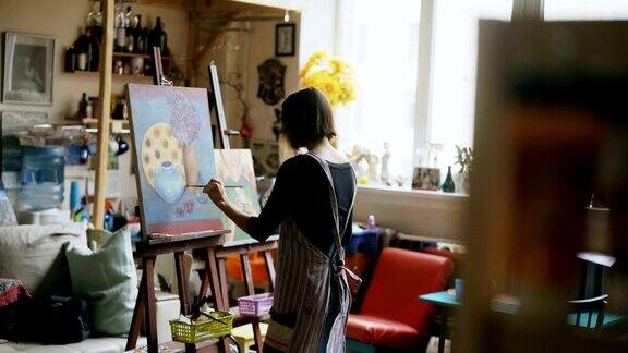 后视图的年轻画家女孩在围裙画静物画在画布上在艺术课