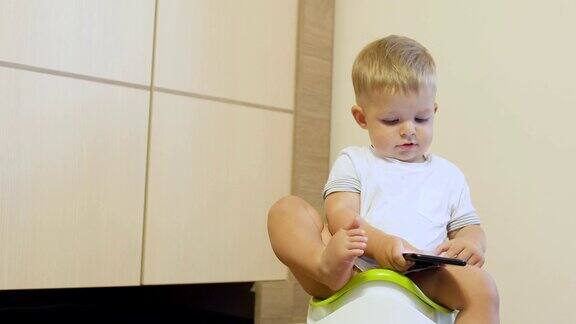 可爱的小男孩坐在便盆上玩手机