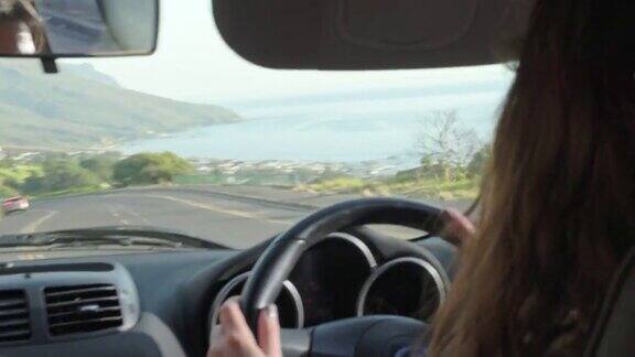 一个年轻的女人开着车沿着海边一条风景优美的道路行驶