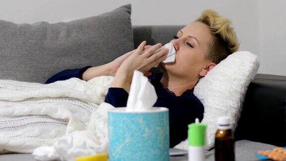 一个生病的年轻女子因感冒坐在家里的沙发上她盖着一条毯子擤着鼻子