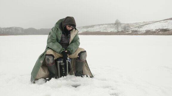 冬季钓鱼渔夫正在冰洞里用鱼竿捕鱼人类在结冰的湖面上钓鱼冬季极端的设备