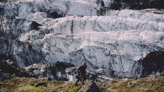 旅行者带着吉他盒沿着冰川旁边的岩石山脊跑步