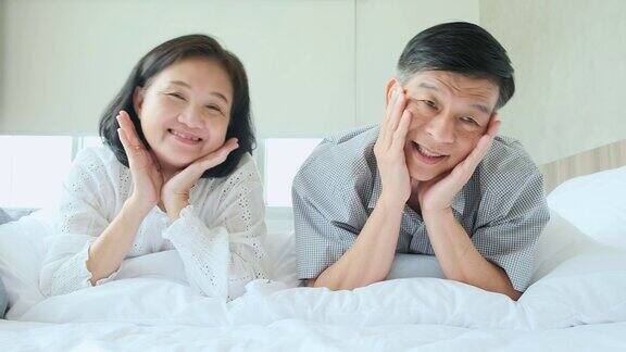 幸福安康健康的老亚洲夫妇一起笑一起享受躺下休闲在床上快乐的老夫妇躺在床上看镜头慢动作