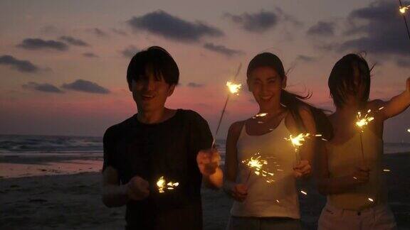 一群朋友在海边的夜晚聚会上玩的孟加拉灯在他们的手青少年们在海滩上用烟花聚会慢动作镜头