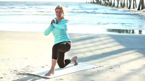 成熟的女人在海滩上做瑜伽练习