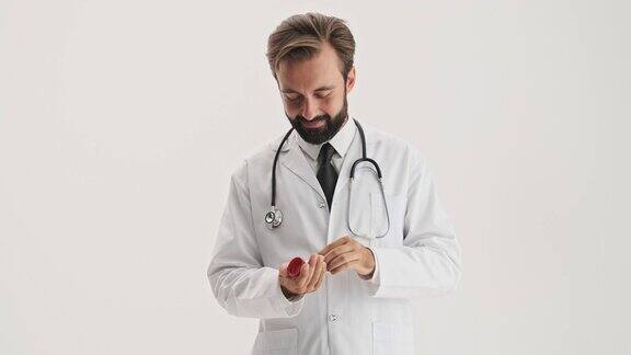 微笑的男医生用听诊器打开了装有药丸的瓶子并把一些药丸放在他的手里
