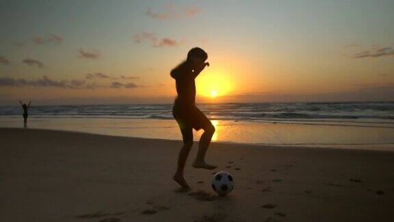 日出时小男孩在沙滩上踢足球